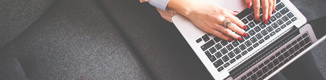Hände tippen auf eine Laptop-Tastatur auf einer dunklen Oberfläche.